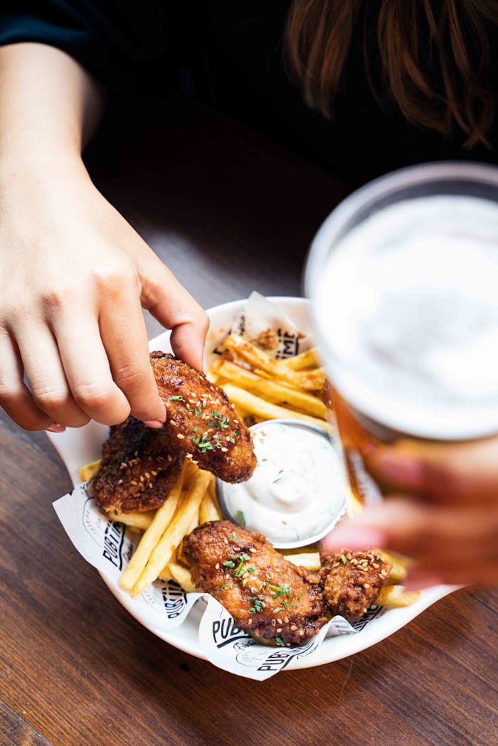 Close-up of hands holding fried chicken and fries with creamy sauce.