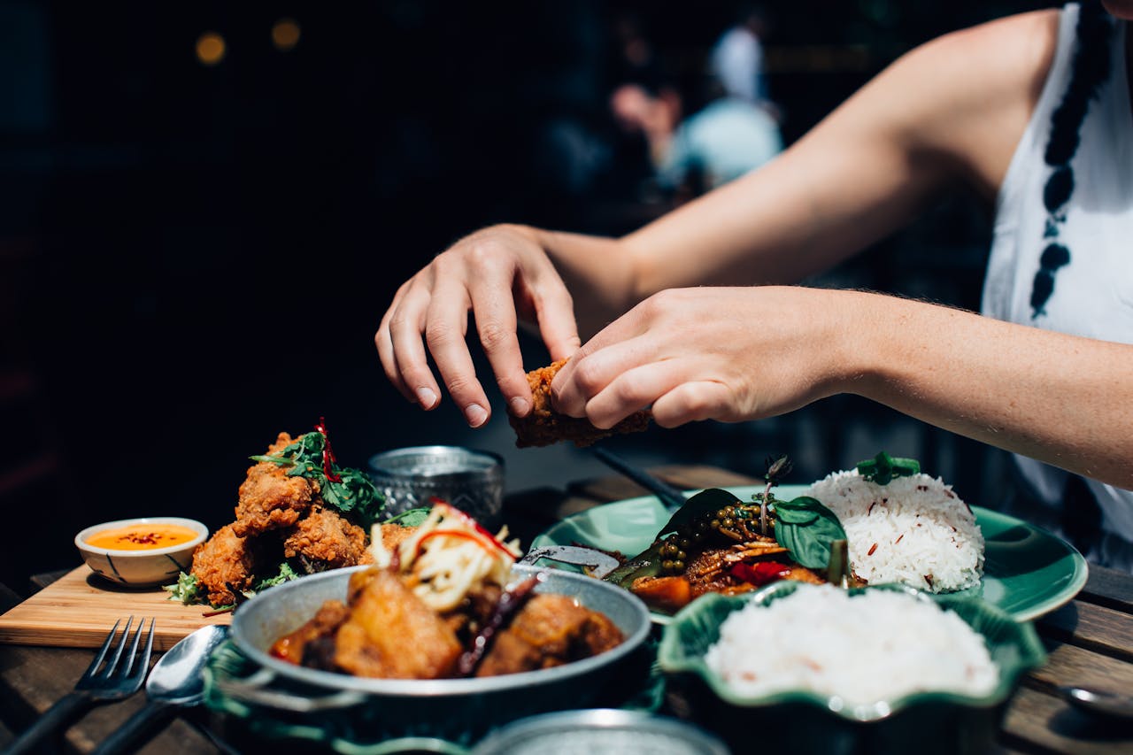 Close-up of a woman's hands enjoying fried chicken and rice outdoors in a restaurant setting.