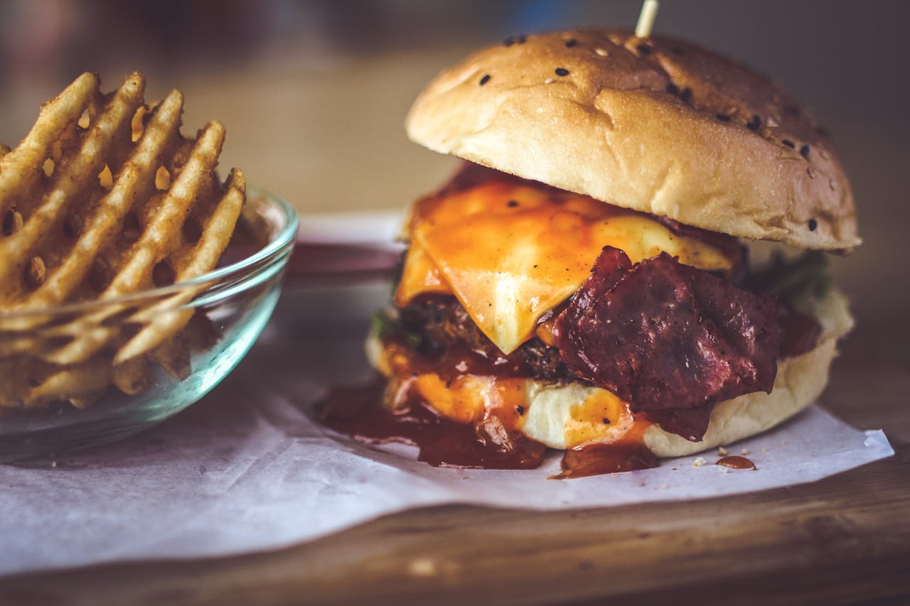 Close-up of a delicious cheeseburger with bacon and sauce, served alongside crispy waffle fries.